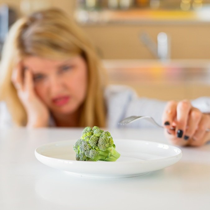 Mulher com dificuldade de comer verdura prejudicando seu início na dieta vegana.