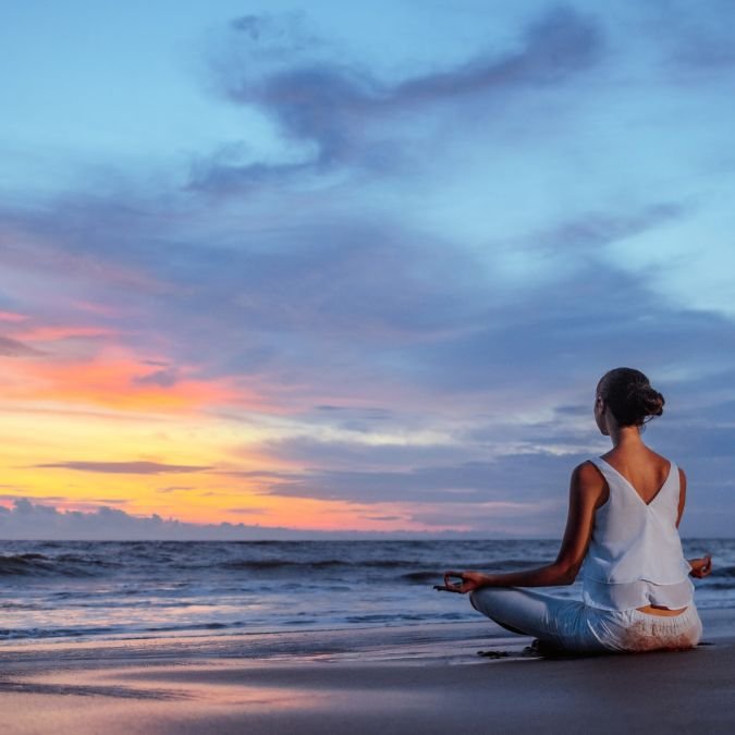 Mulher meditando na praia ao pôr do sol, indicando desconexão digital