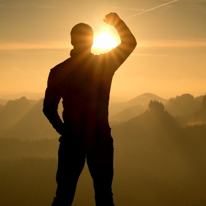 Atleta confiante apreciando o pôr do sol no alto da montanha.