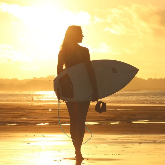 Uma surfista andando na praia ao pôr do sol.