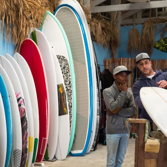 Vendedor mostrando a variedade de pranchas pra um surfista iniciante.