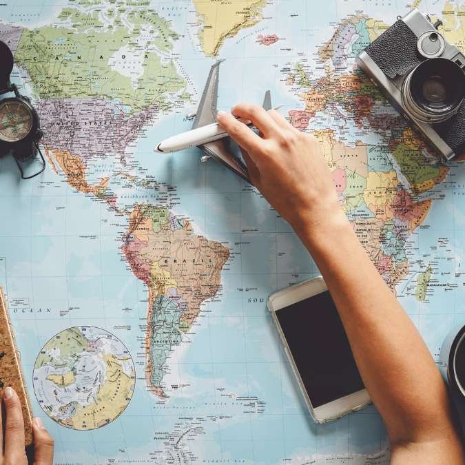 Mão segurando um avião miniatura em um mapa mundi.